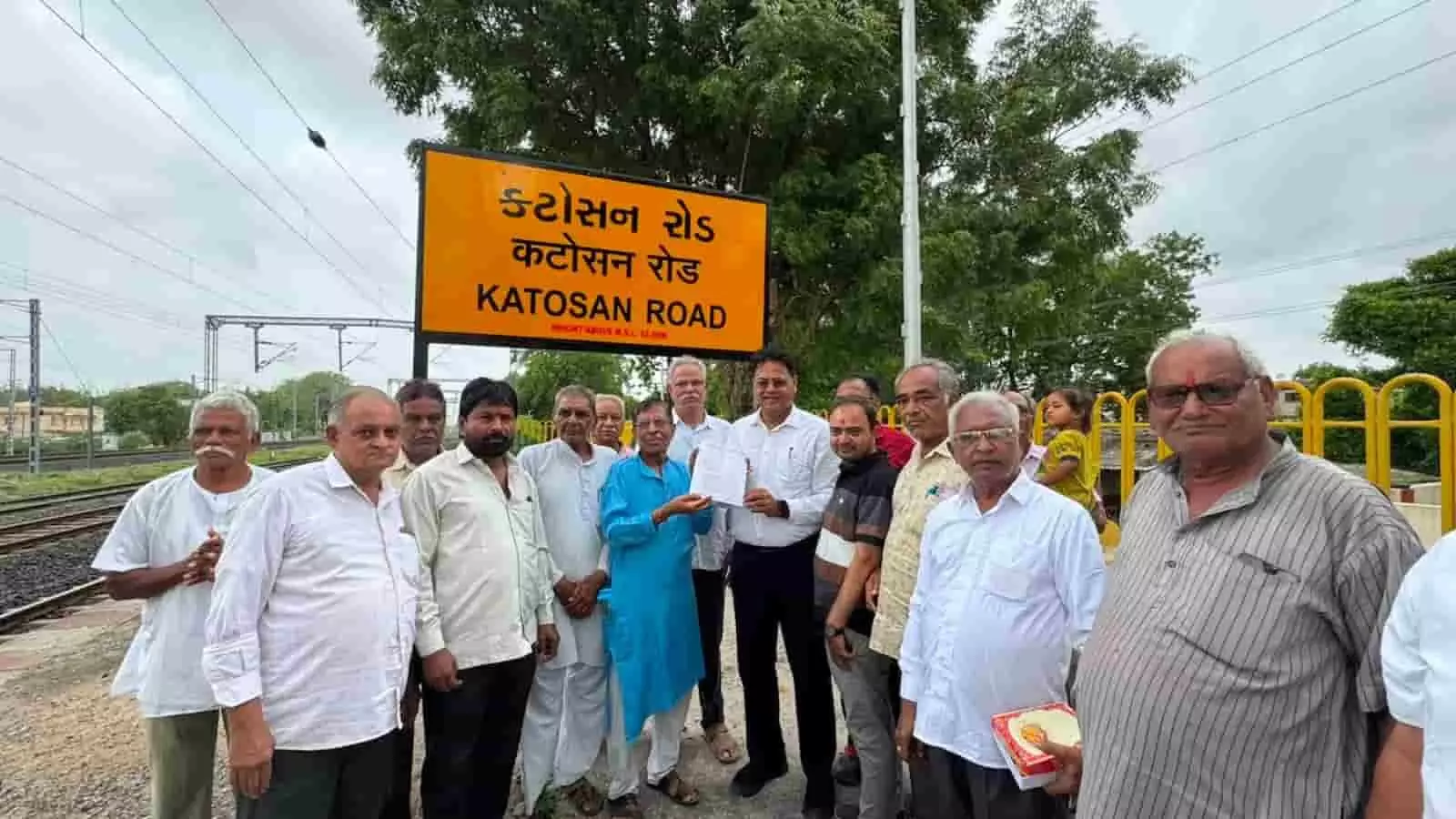 कटोसन रोड रेलवे स्टेशन के पीले बोर्ड के सामने स्थानीय जनप्रतिनिधि और रेलवे अधिकारियों का समूह। कटोसन रोड रेलवे स्टेशन के पीले बोर्ड के सामने स्थानीय जनप्रतिनिधि और रेलवे अधिकारियों का समूह।