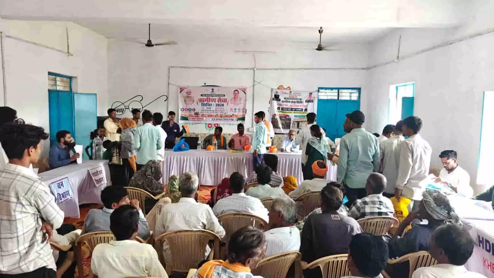 ग्रामीण सेवा शिविर के दौरान हॉल में अधिकारियों के सामने कुर्सियों पर बैठे ग्रामीण। ग्रामीण सेवा शिविर के दौरान हॉल में अधिकारियों के सामने कुर्सियों पर बैठे ग्रामीण।