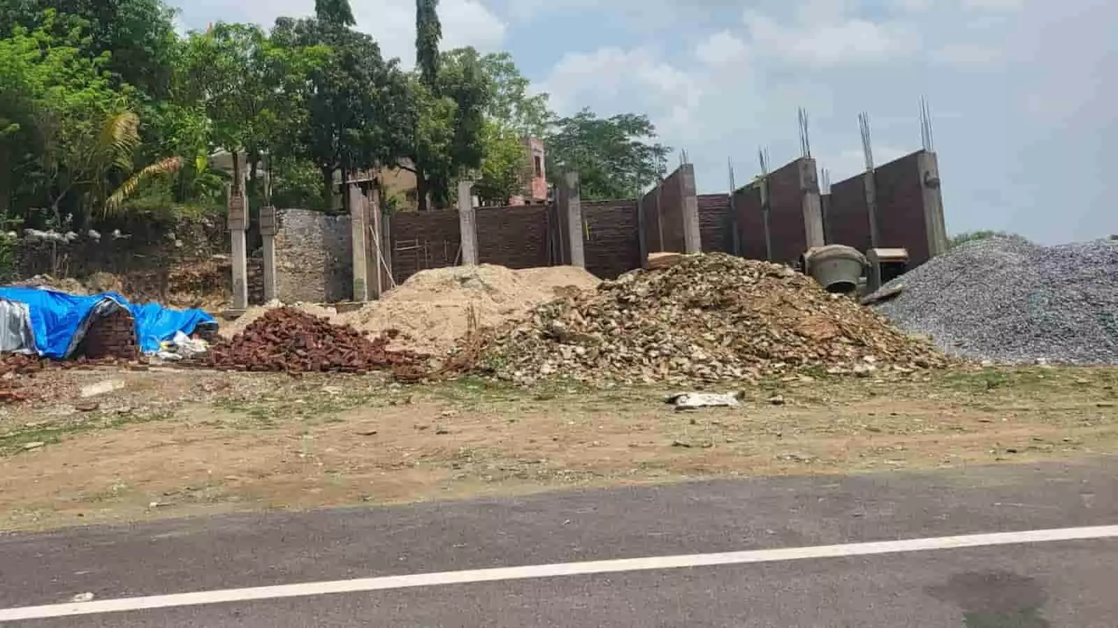 राष्ट्रीय राजमार्ग के किनारे निर्माण सामग्री और निर्माणाधीन दीवार दिखाई दे रही है। राष्ट्रीय राजमार्ग के किनारे निर्माण सामग्री और निर्माणाधीन दीवार दिखाई दे रही है।