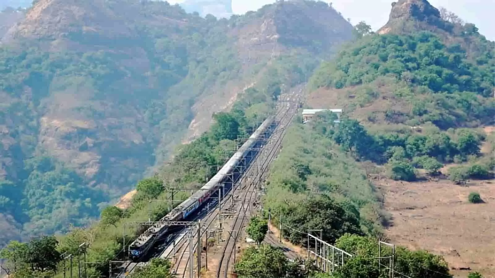 हरी-भरी पहाड़ियों के बीच रेलवे ट्रैक पर गुजरती हुई एक रेलगाड़ी। हरी-भरी पहाड़ियों के बीच रेलवे ट्रैक पर गुजरती हुई एक रेलगाड़ी।