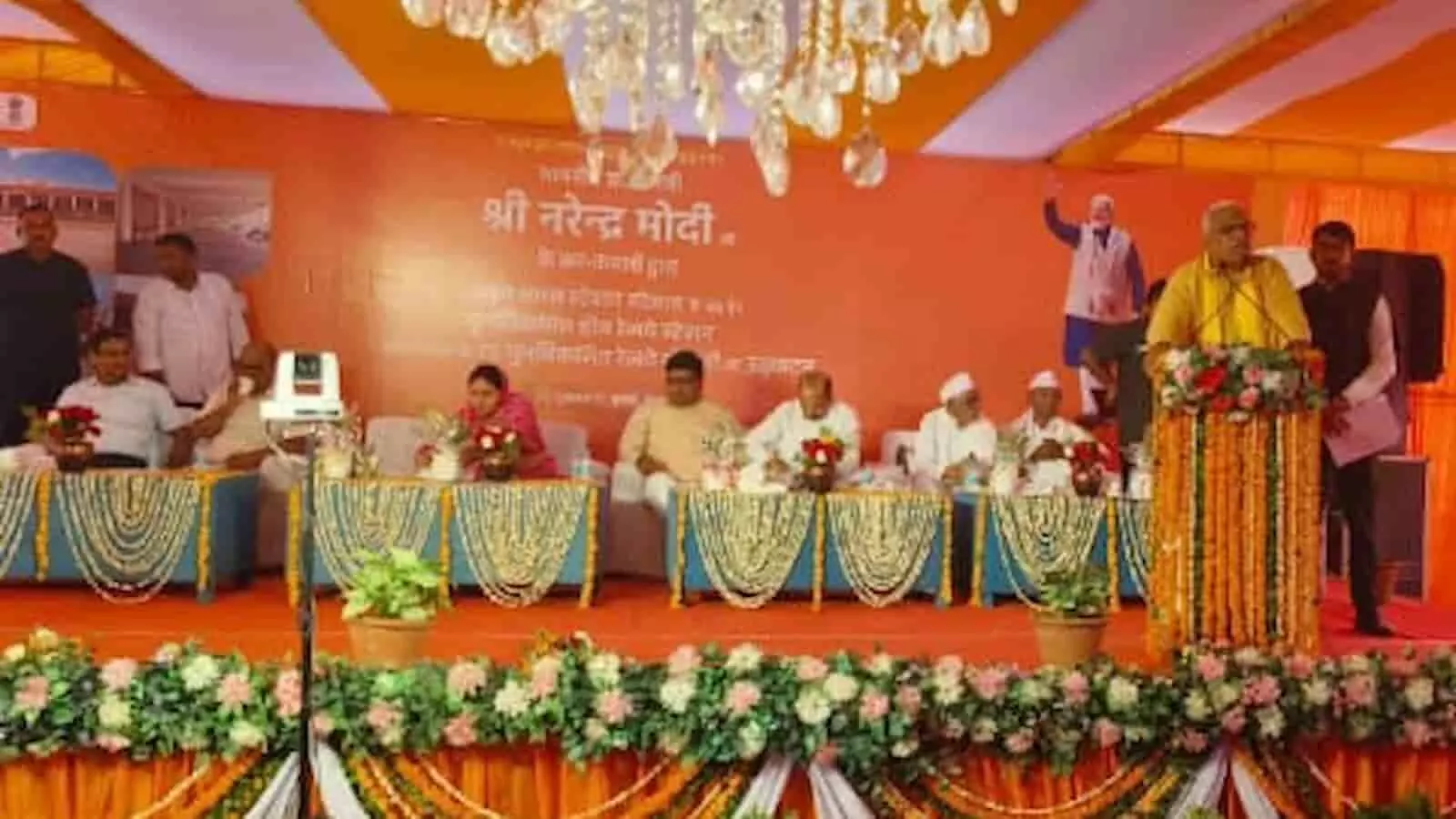 फूलों से सजे मंच पर पोडियम से भाषण देते एक व्यक्ति और बैठे हुए अतिथि समारोह में फूलों से सजे मंच पर पोडियम से भाषण देते एक व्यक्ति और बैठे हुए अतिथि समारोह में