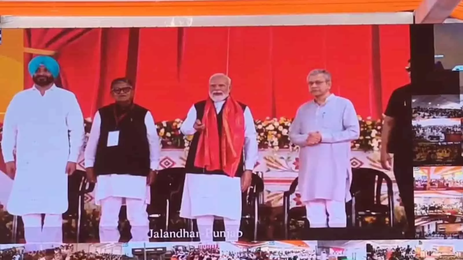 बड़ी स्क्रीन पर जालंधर कैंट में मंच पर खड़े प्रधानमंत्री नरेन्द्र मोदी और अन्य केंद्रीय मंत्री। बड़ी स्क्रीन पर जालंधर कैंट में मंच पर खड़े प्रधानमंत्री नरेन्द्र मोदी और अन्य केंद्रीय मंत्री।