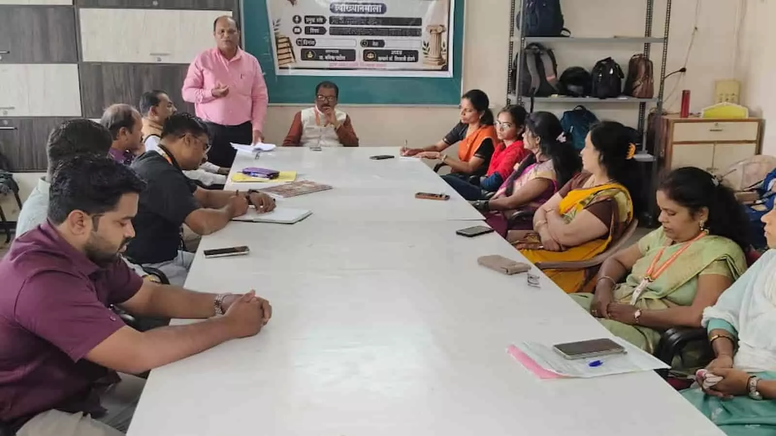 व्याख्यान कक्ष में मेज के पास बैठकर व्याख्यान सुनते प्राध्यापक और संबोधित करते वक्ता। व्याख्यान कक्ष में मेज के पास बैठकर व्याख्यान सुनते प्राध्यापक और संबोधित करते वक्ता।