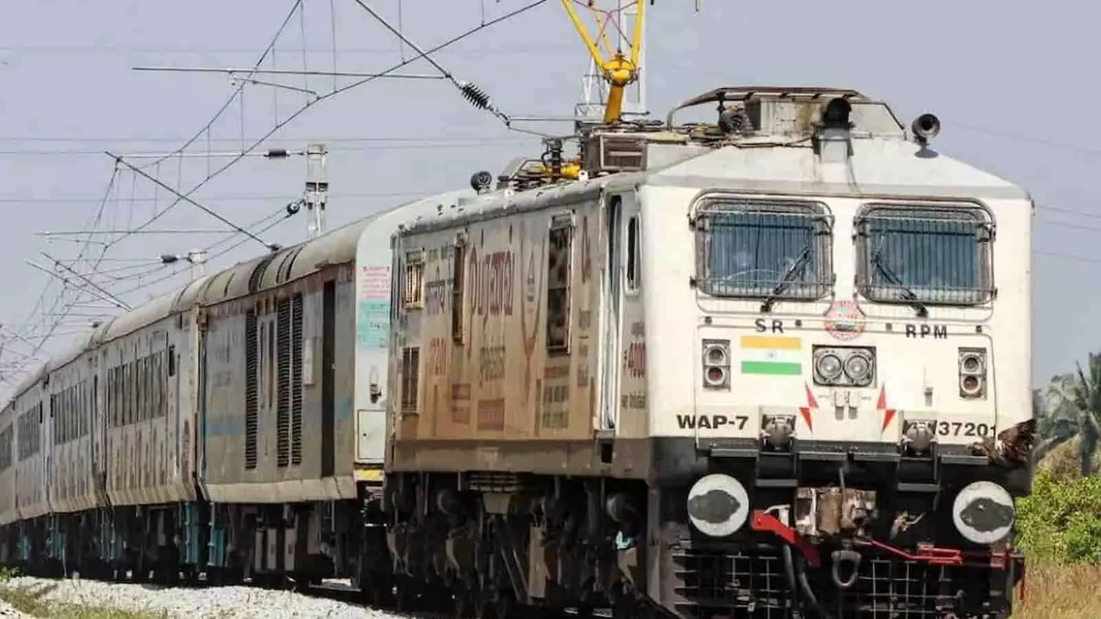 इलेक्ट्रिक इंजन वाली एक यात्री ट्रेन पटरी पर तेजी से दौड़ रही है।