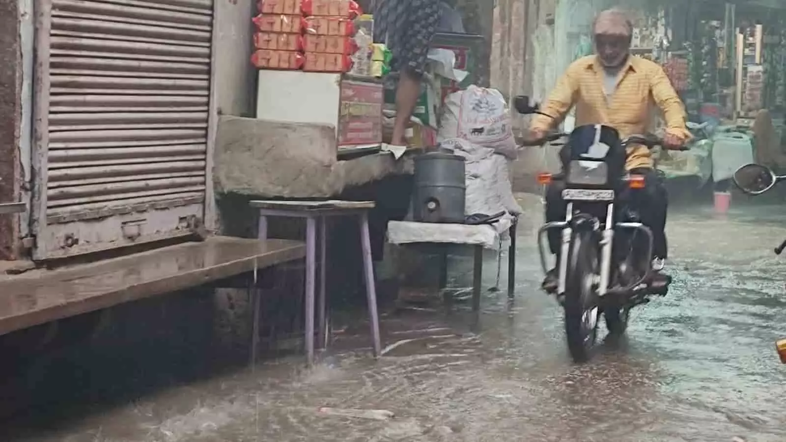 जलभराव वाली सड़क पर मोटरसाइकिल चलाता एक व्यक्ति जो बारिश के बाद जलजमाव को दर्शाता है। जलभराव वाली सड़क पर मोटरसाइकिल चलाता एक व्यक्ति जो बारिश के बाद जलजमाव को दर्शाता है।