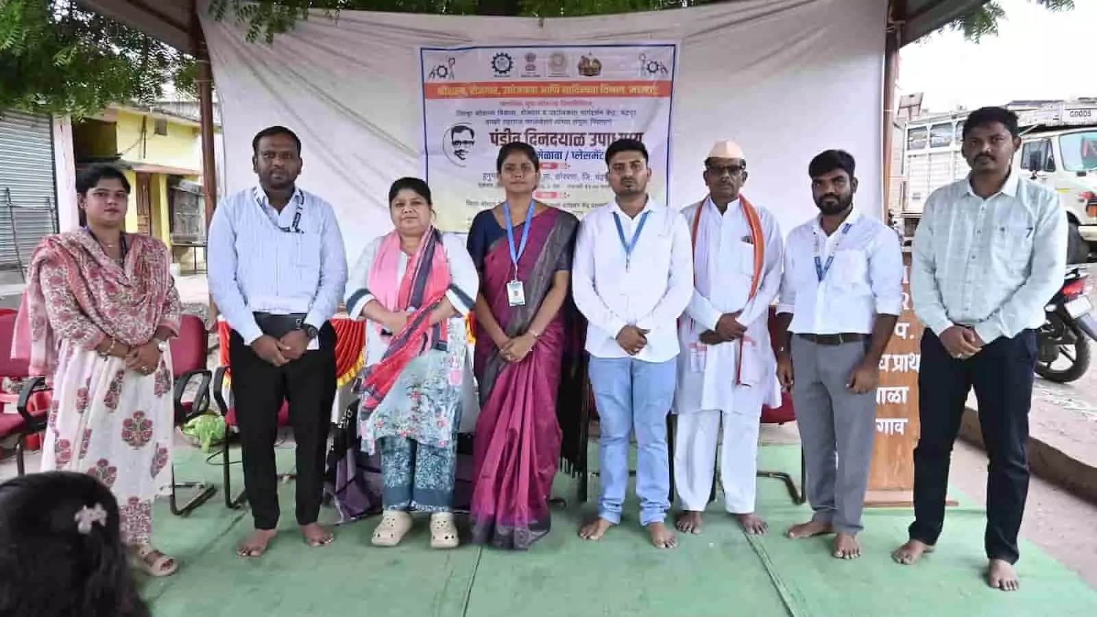तस्वीर में मंच पर आठ लोग वडगाव में कार्यक्रम के दौरान समूह फोटो के लिए खड़े हैं। तस्वीर में मंच पर आठ लोग वडगाव में कार्यक्रम के दौरान समूह फोटो के लिए खड़े हैं।