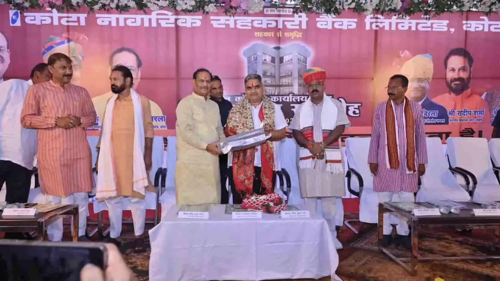 कोटा नागरिक सहकारी बैंक शिलान्यास समारोह में मंच पर खड़े अतिथि नजर आ रहे हैं।