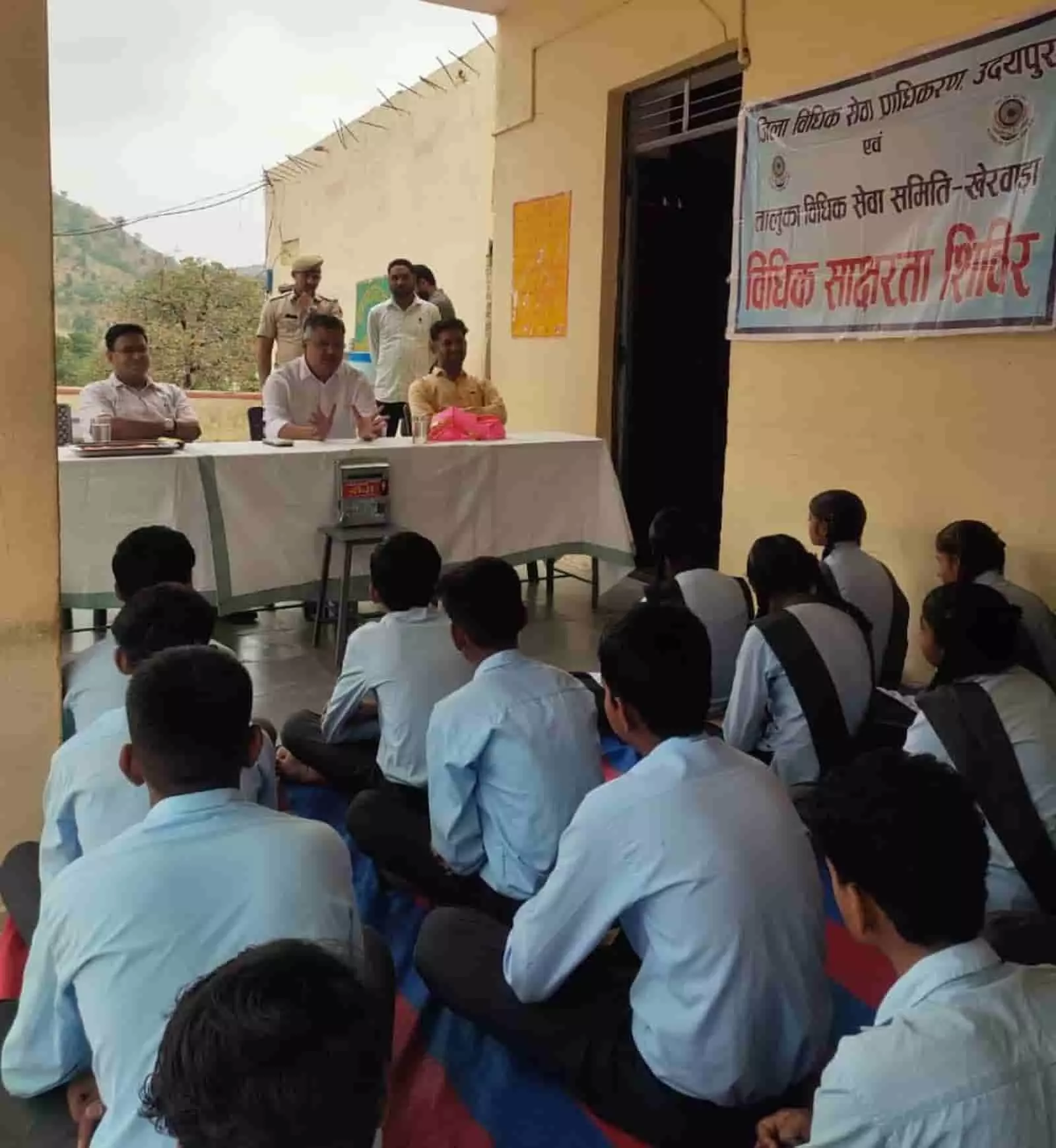 विधिक साक्षरता शिविर में जमीन पर बैठे विद्यार्थियों को संबोधित करते न्यायिक अधिकारी। विधिक साक्षरता शिविर में जमीन पर बैठे विद्यार्थियों को संबोधित करते न्यायिक अधिकारी।