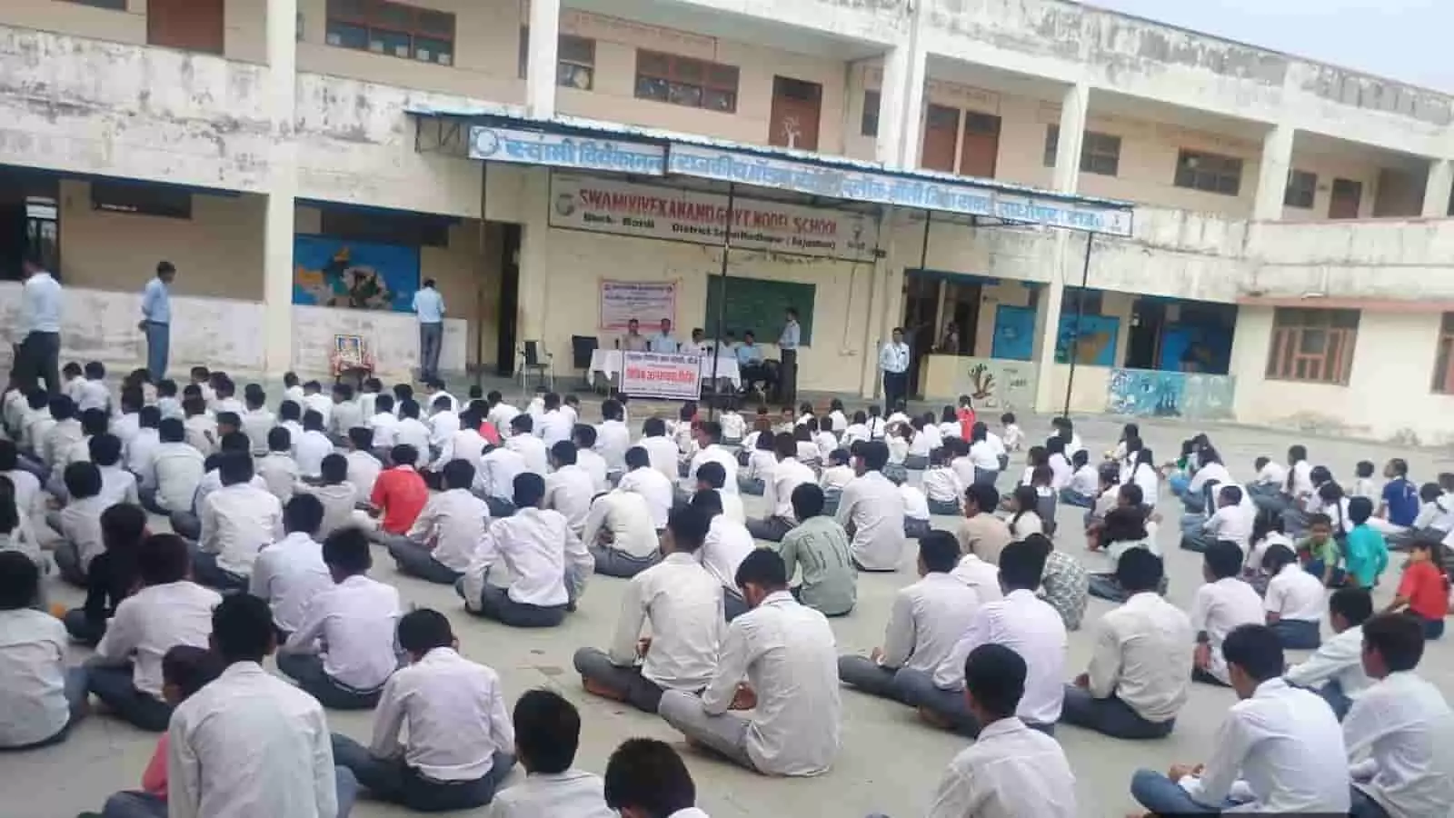 स्कूल परिसर में जमीन पर बैठकर विधिक जागरूकता शिविर में भाग लेते हुए विद्यार्थी। स्कूल परिसर में जमीन पर बैठकर विधिक जागरूकता शिविर में भाग लेते हुए विद्यार्थी।