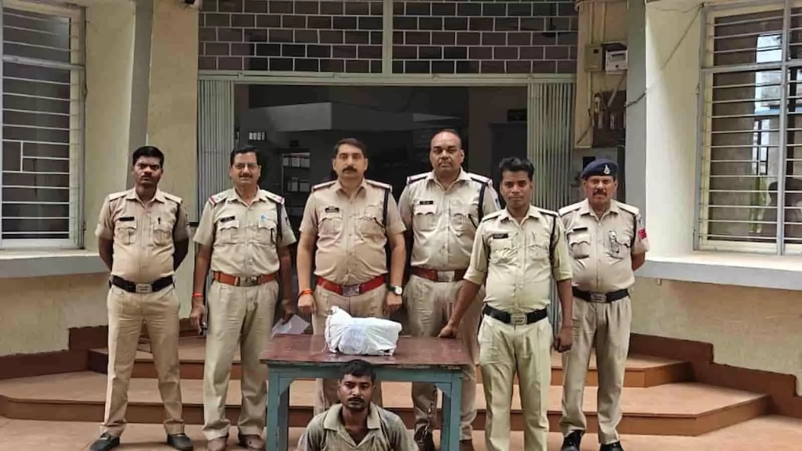 तस्वीर में कुठला थाने के सामने पुलिस अधिकारियों के साथ खड़ा आरोपी और टेबल पर रखा गांजा। तस्वीर में कुठला थाने के सामने पुलिस अधिकारियों के साथ खड़ा आरोपी और टेबल पर रखा गांजा।