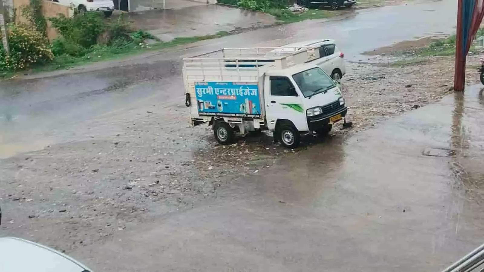 बारिश में भीगी सड़क पर खड़े वाहन और जलभराव का दृश्य दिखाई दे रहा है। बारिश में भीगी सड़क पर खड़े वाहन और जलभराव का दृश्य दिखाई दे रहा है।
