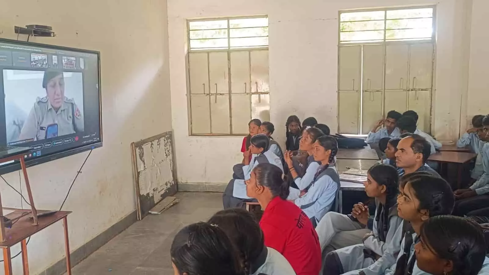 तस्वीर में कमरे में बैठे विद्यार्थी और शिक्षक डिजिटल स्क्रीन पर महिला पुलिस अधिकारी को सुनते हुए। तस्वीर में कमरे में बैठे विद्यार्थी और शिक्षक डिजिटल स्क्रीन पर महिला पुलिस अधिकारी को सुनते हुए।