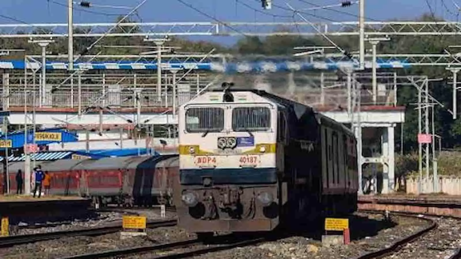 तस्वीर में रेलवे स्टेशन के ट्रैक पर ट्रेन और उसका इंजन खड़ा दिखाई दे रहा है।