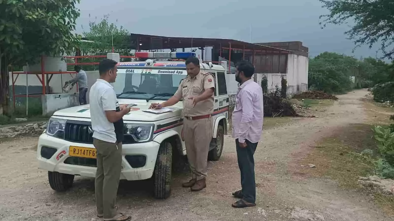 तस्वीर में एक पुलिसकर्मी राजस्थान पुलिस की गाड़ी के पास खड़े दो लोगों से बातचीत कर रहा है।