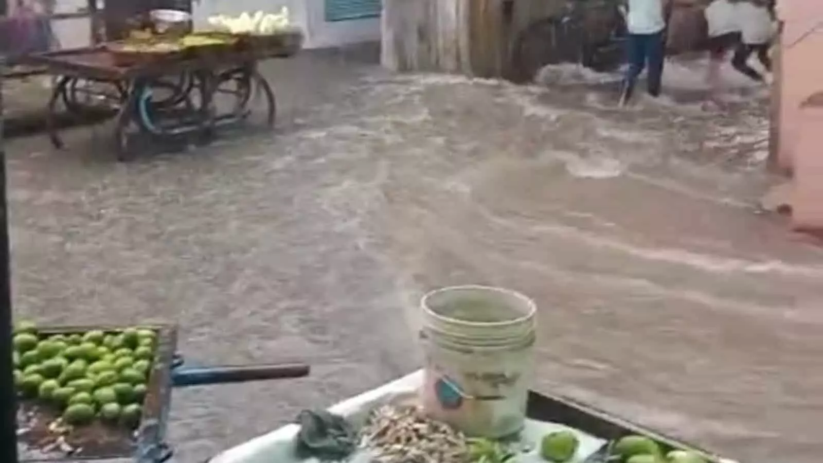 कानोड़ की जलमग्न सड़क पर बहते पानी और किनारे रखे ठेलों का दृश्य।