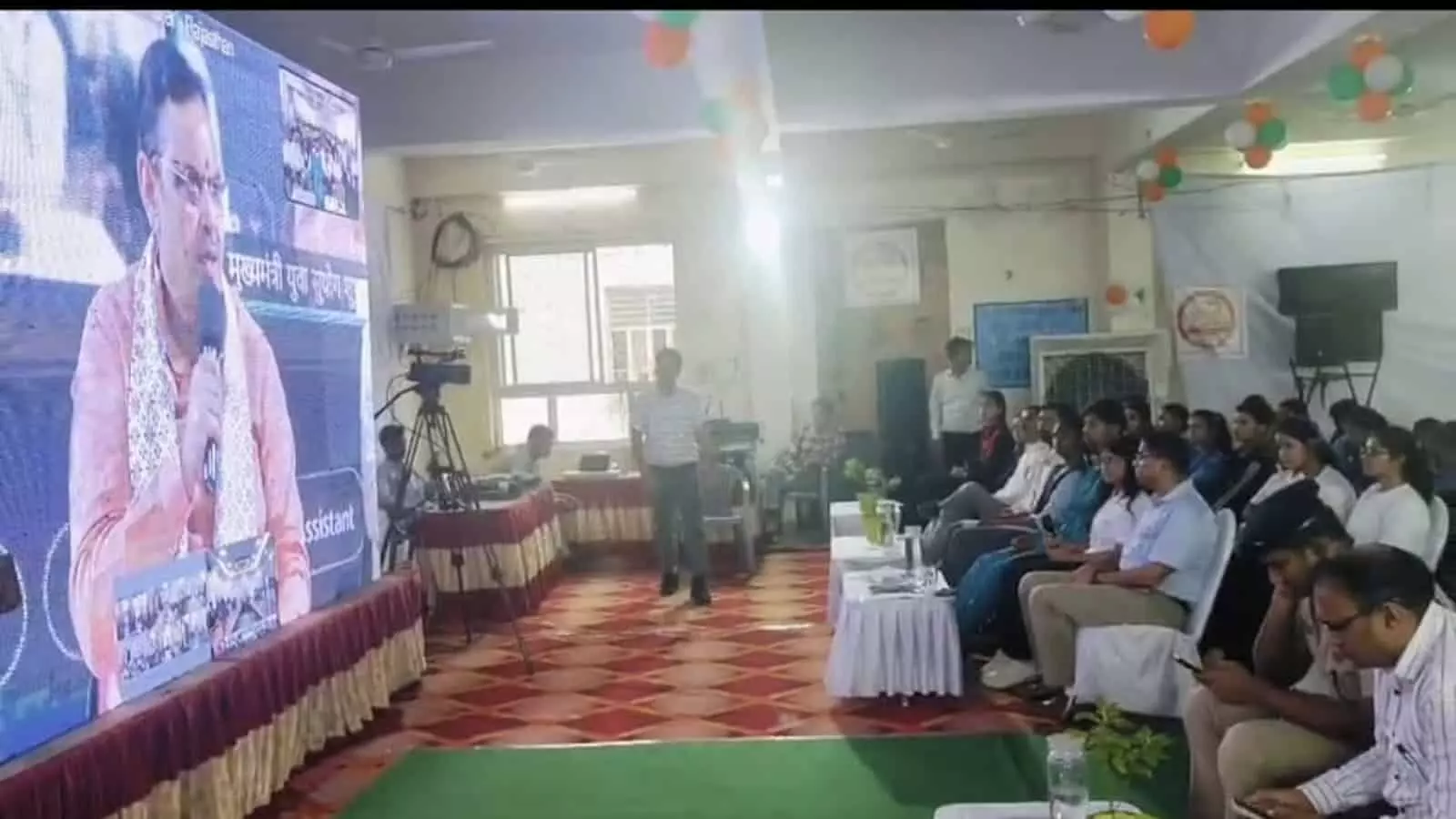 जिला परिषद सभागार बारां में मुख्यमंत्री युवा सुयोग योजना के शुभारंभ कार्यक्रम के दौरान बड़ी स्क्रीन पर जुड़े मुख्यमंत्री का संबोधन देखते अधिकारी और युवा।