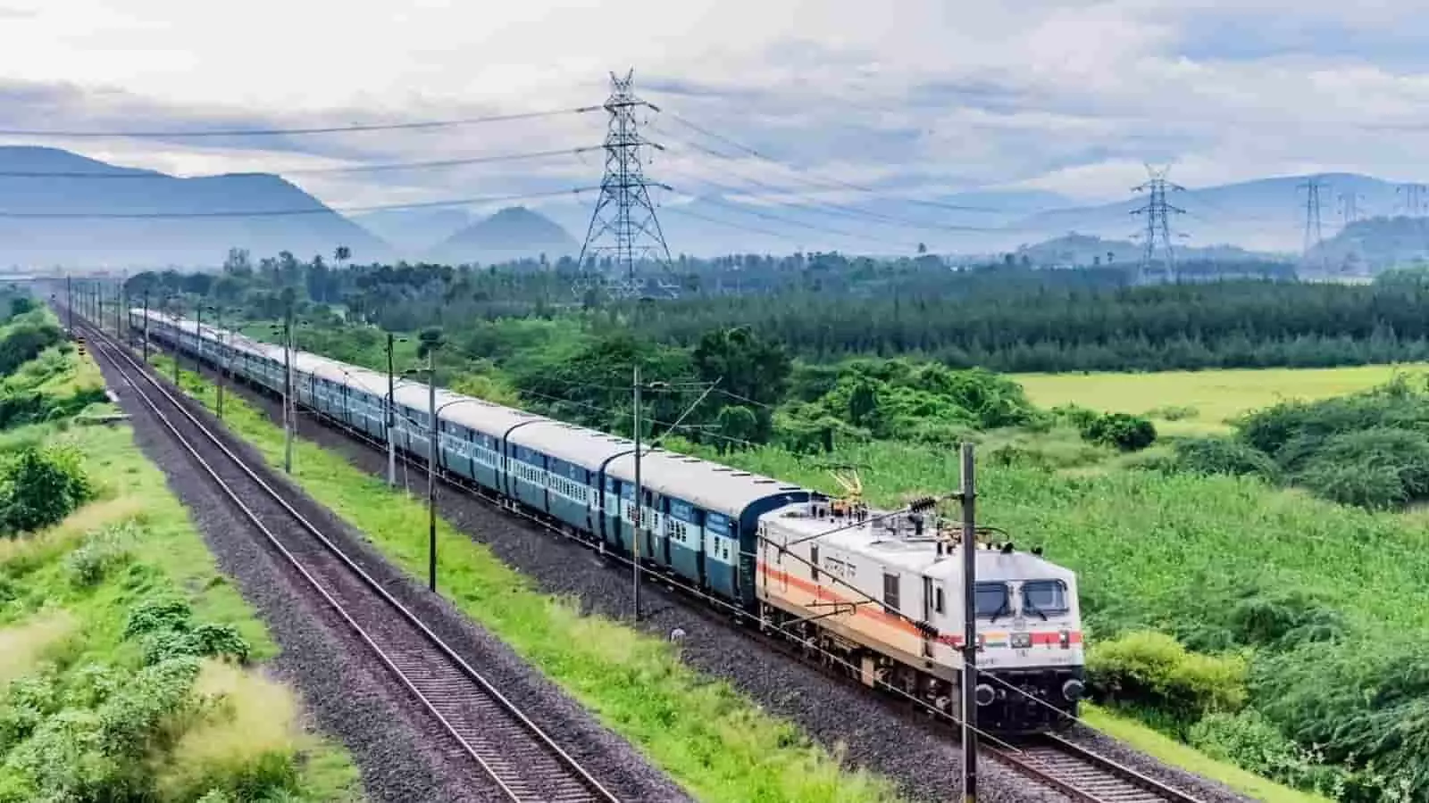तस्वीर में पटरियों पर दौड़ती एक भारतीय रेल ट्रेन और आसपास हरे-भरे खेत दिखाई दे रहे हैं। तस्वीर में पटरियों पर दौड़ती एक भारतीय रेल ट्रेन और आसपास हरे-भरे खेत दिखाई दे रहे हैं।
