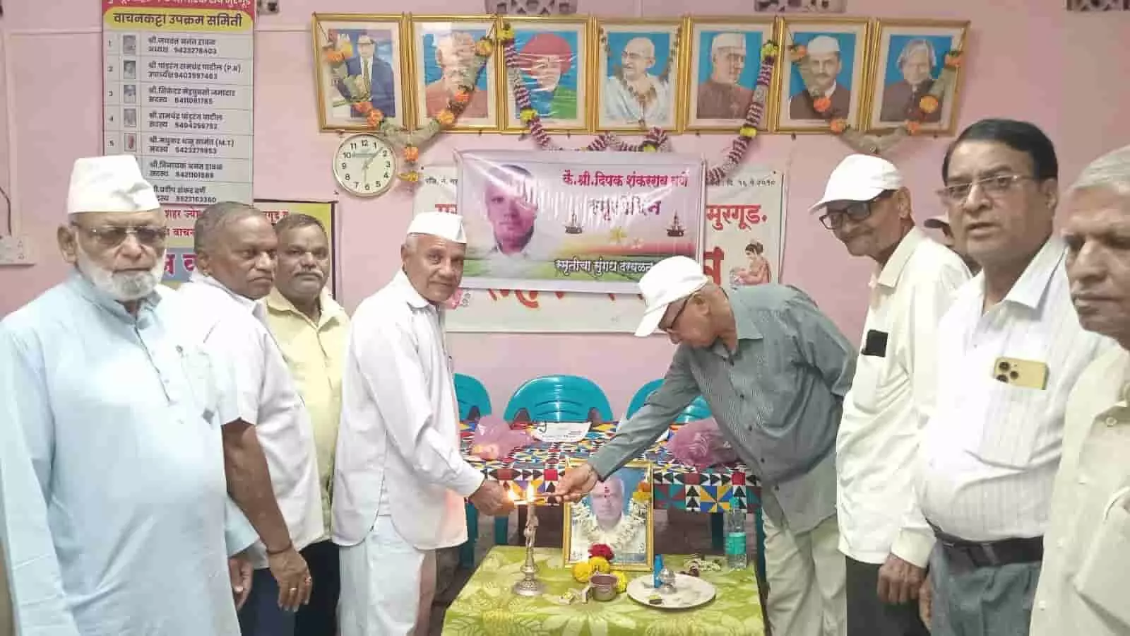 हॉल में एक तस्वीर के सामने दीपक जलाते बुजुर्ग और खड़े लोग। हॉल में एक तस्वीर के सामने दीपक जलाते बुजुर्ग और खड़े लोग।
