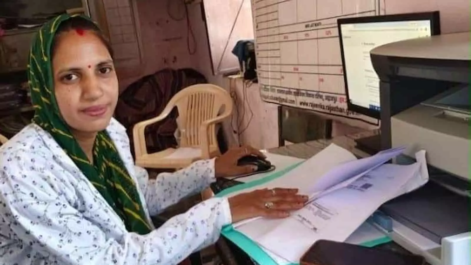 तस्वीर में एक महिला कार्यालय में मेज पर दस्तावेज और कंप्यूटर के पास बैठी हुई है। तस्वीर में एक महिला कार्यालय में मेज पर दस्तावेज और कंप्यूटर के पास बैठी हुई है।