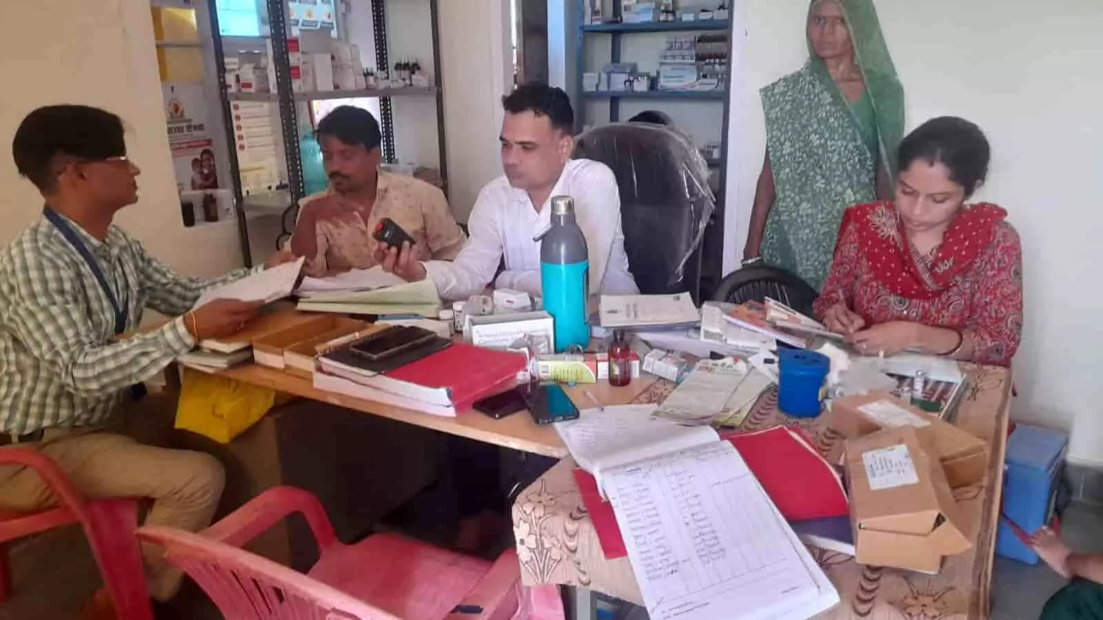 तस्वीर में उप स्वास्थ्य केंद्र के कमरे में स्वास्थ्य अधिकारी और कर्मचारी मेज पर रखे रजिस्टरों की जांच करते दिख रहे हैं। तस्वीर में उप स्वास्थ्य केंद्र के कमरे में स्वास्थ्य अधिकारी और कर्मचारी मेज पर रखे रजिस्टरों की जांच करते दिख रहे हैं।