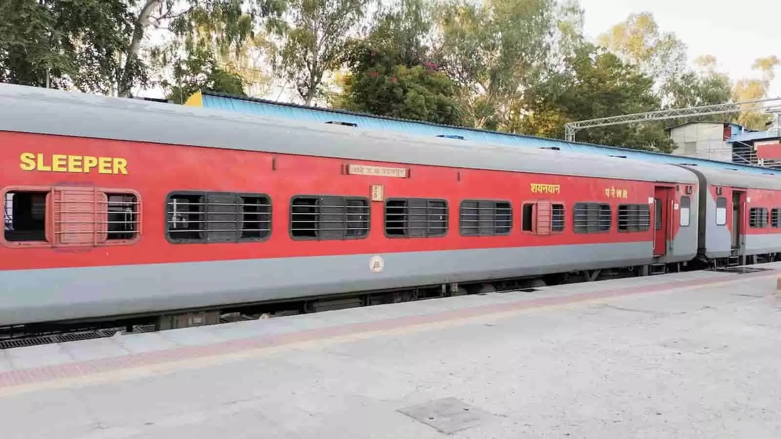 तस्वीर में रेलवे स्टेशन पर खड़ी एक लाल और ग्रे रंग की ट्रेन का कोच दिख रहा है। तस्वीर में रेलवे स्टेशन पर खड़ी एक लाल और ग्रे रंग की ट्रेन का कोच दिख रहा है।