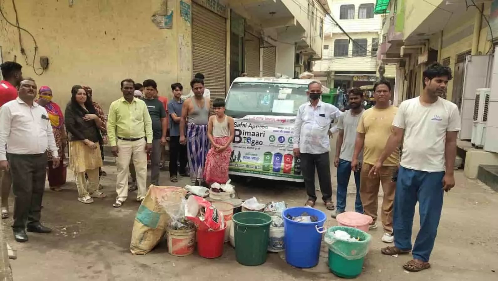 तस्वीर में संजय नगर भट्टा बस्ती की गली में खड़े लोग, विभिन्न रंग के डस्टबिन और स्वच्छता वाहन दिखाई दे रहे हैं। तस्वीर में संजय नगर भट्टा बस्ती की गली में खड़े लोग, विभिन्न रंग के डस्टबिन और स्वच्छता वाहन दिखाई दे रहे हैं।