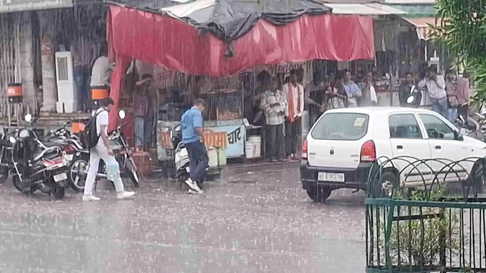 बारिश के दौरान चित्तौड़गढ़ में सड़क पर चलते लोग और दुकान के नीचे खड़े नागरिक। बारिश के दौरान चित्तौड़गढ़ में सड़क पर चलते लोग और दुकान के नीचे खड़े नागरिक।