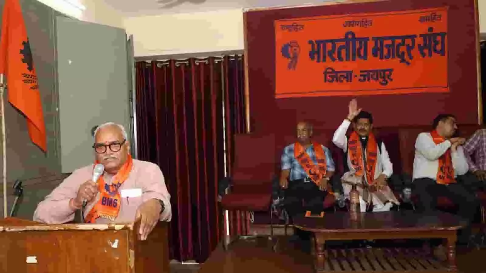 तस्वीर में भारतीय मजदूर संघ के कार्यक्रम में पोडियम पर संबोधन देते पदाधिकारी और मंच पर मौजूद लोग। तस्वीर में भारतीय मजदूर संघ के कार्यक्रम में पोडियम पर संबोधन देते पदाधिकारी और मंच पर मौजूद लोग।