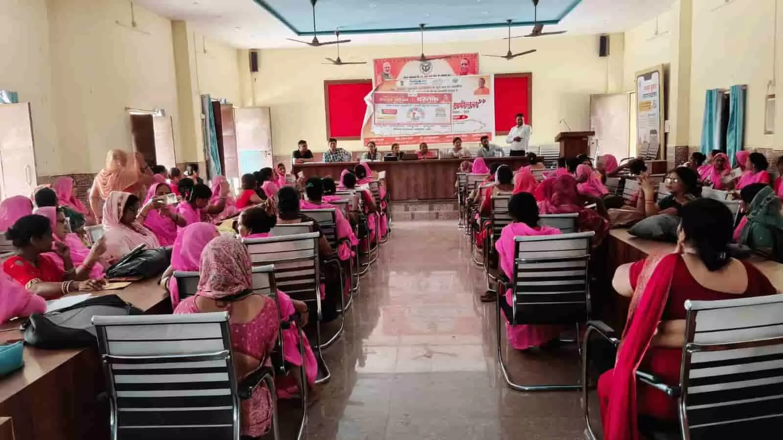 सभागार में बैठक के दौरान कुर्सियों पर बैठी आंगनबाड़ी महिलाएं अलीगंज में।