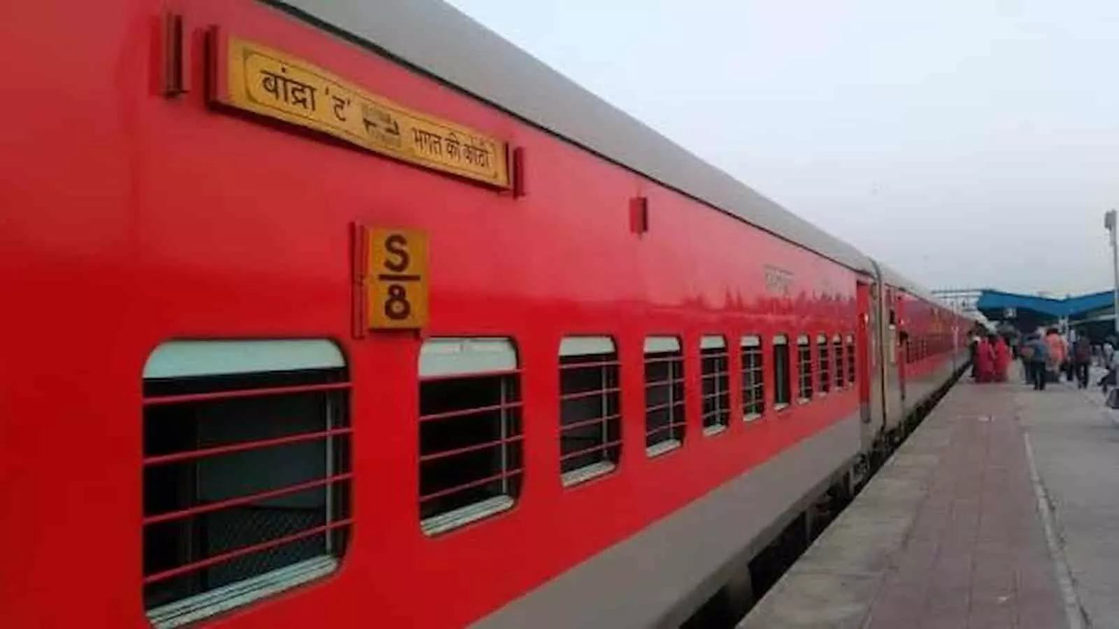 तस्वीर में प्लेटफॉर्म पर खड़ी लाल रंग की यात्री ट्रेन और आसपास मौजूद यात्री दिखाई दे रहे हैं। तस्वीर में प्लेटफॉर्म पर खड़ी लाल रंग की यात्री ट्रेन और आसपास मौजूद यात्री दिखाई दे रहे हैं।