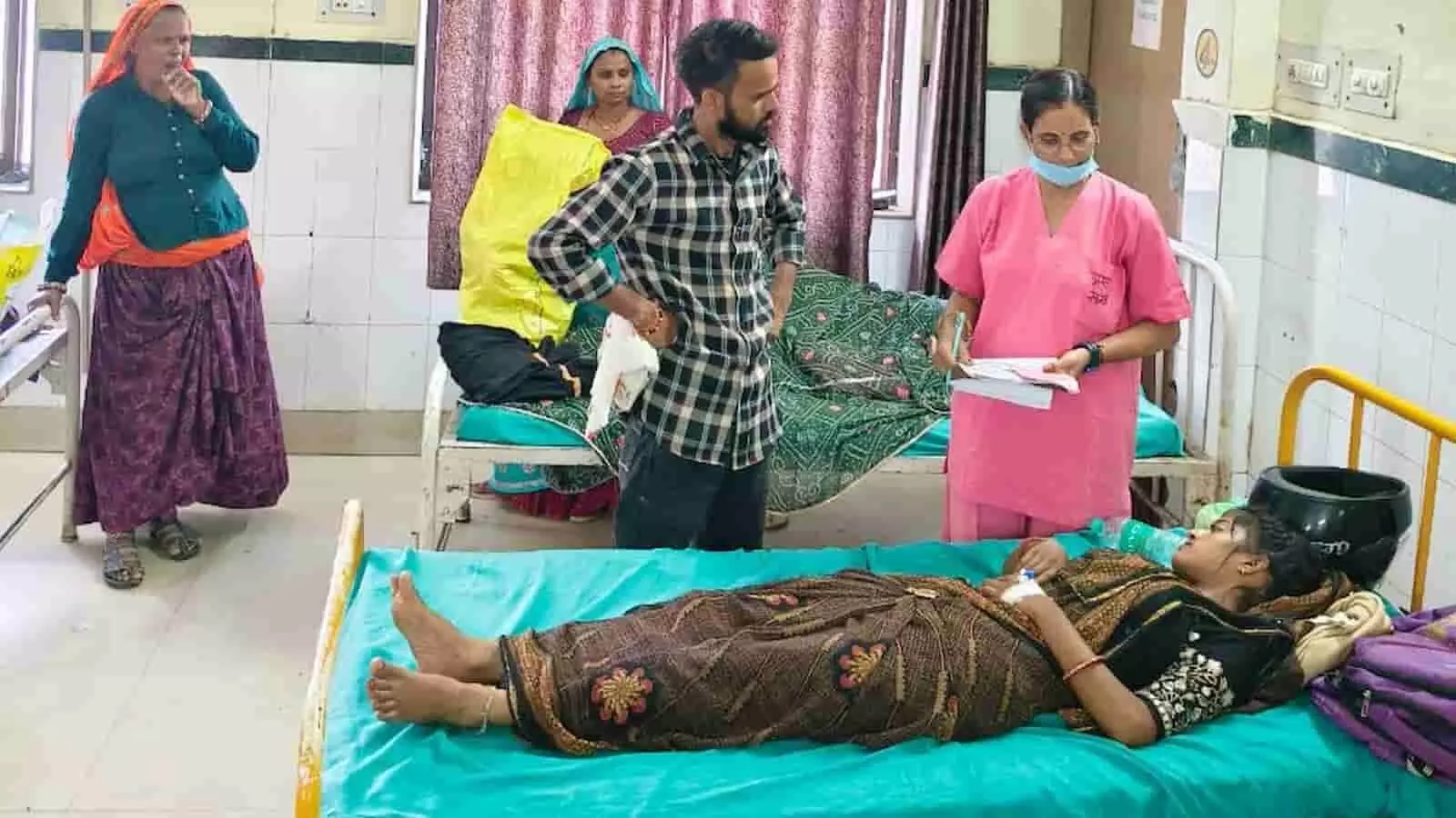 जिला चिकित्सालय के वार्ड में बिस्तर पर लेटी महिला मरीज और पास में मौजूद चिकित्सा कर्मी।