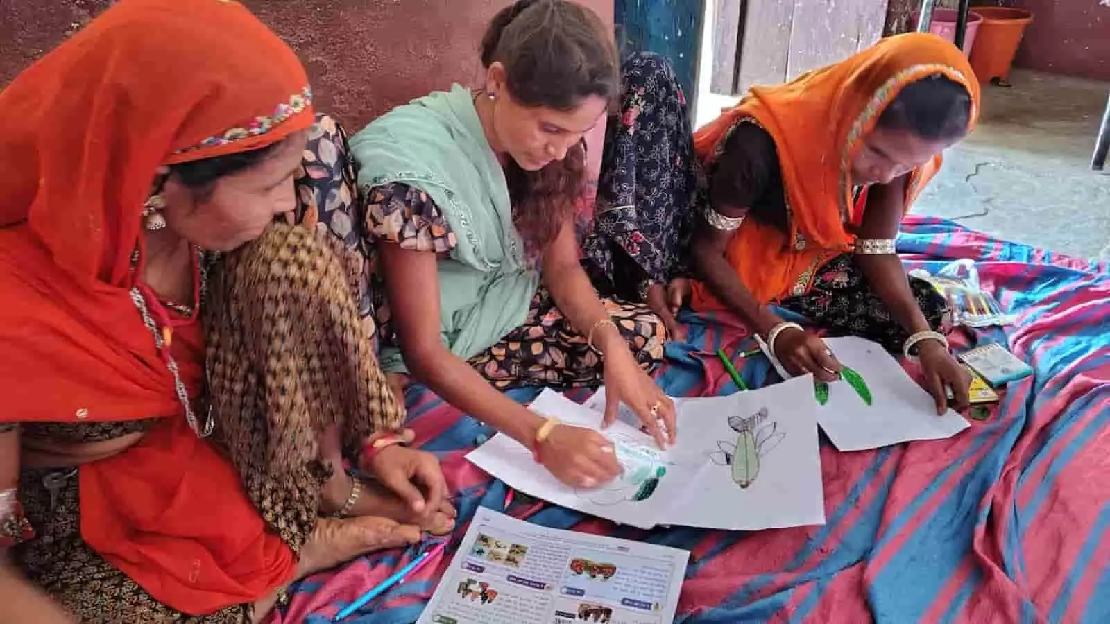 तस्वीर में तीन महिलाएं जमीन पर बैठकर कागज पर चित्रकारी करती हुई दिख रही हैं। तस्वीर में तीन महिलाएं जमीन पर बैठकर कागज पर चित्रकारी करती हुई दिख रही हैं।