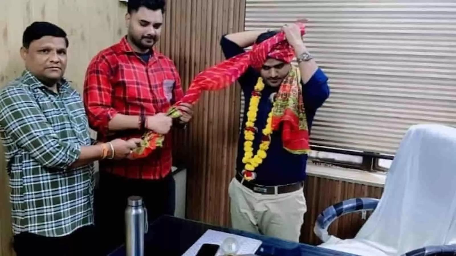 तस्वीर में तीन लोग कार्यालय के कमरे में सहायक नगर नियोजक को साफा पहनाते दिख रहे हैं।