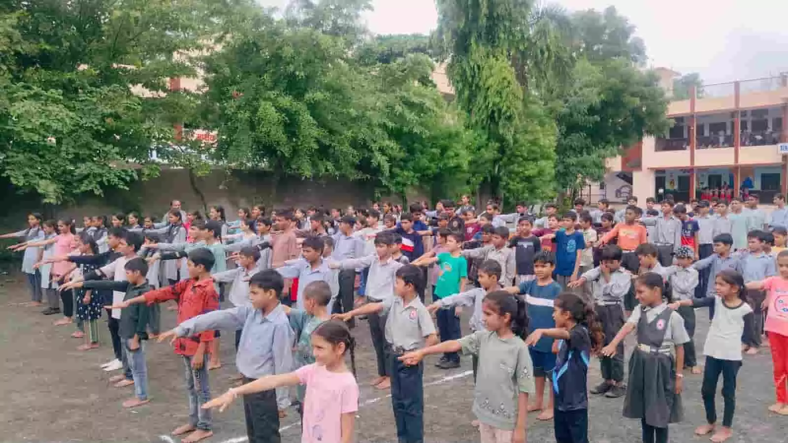 तस्वीर में स्कूल परिसर के खुले मैदान में कतारों में खड़े छात्र-छात्राएं शपथ ले रहे हैं।