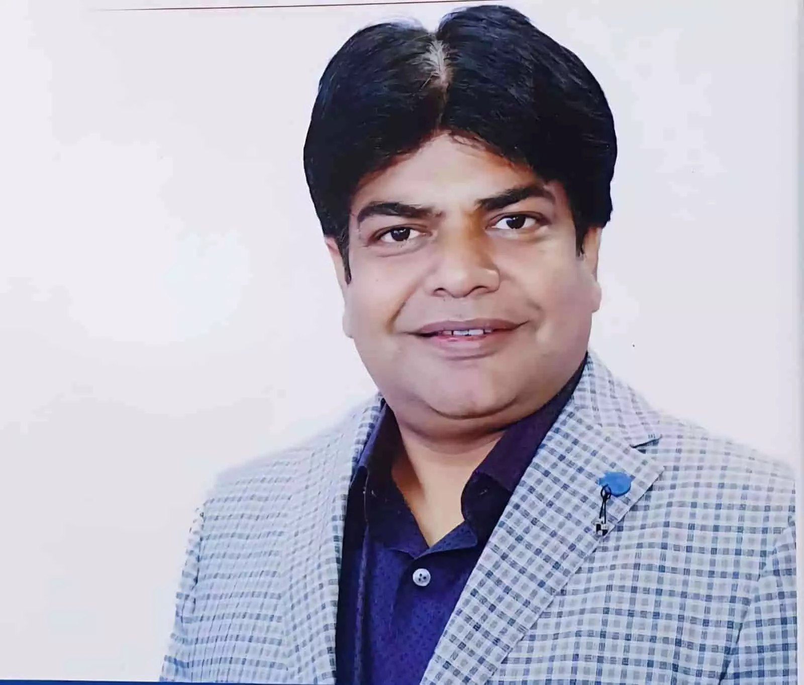 सादे पृष्ठभूमि के सामने चेक्ड ब्लेज़र पहने खड़े डॉ सुमीत गर्ग।