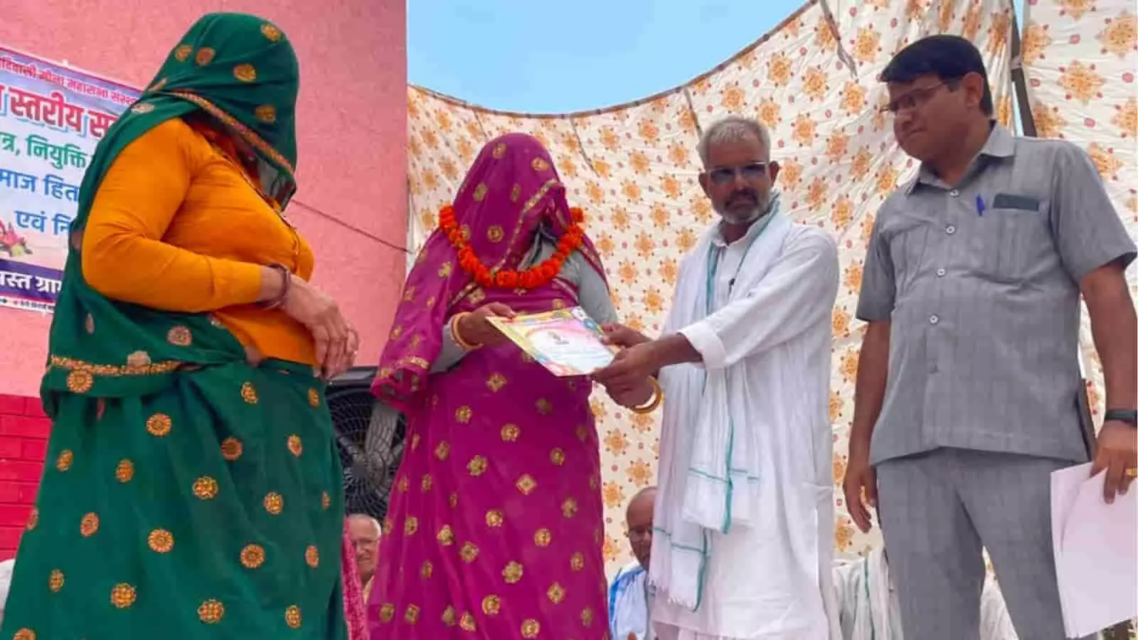 तस्वीर में स्टेज पर पारंपरिक वेशभूषा में महिला को प्रमाण पत्र प्रदान करते हुए लोग दिख रहे हैं।