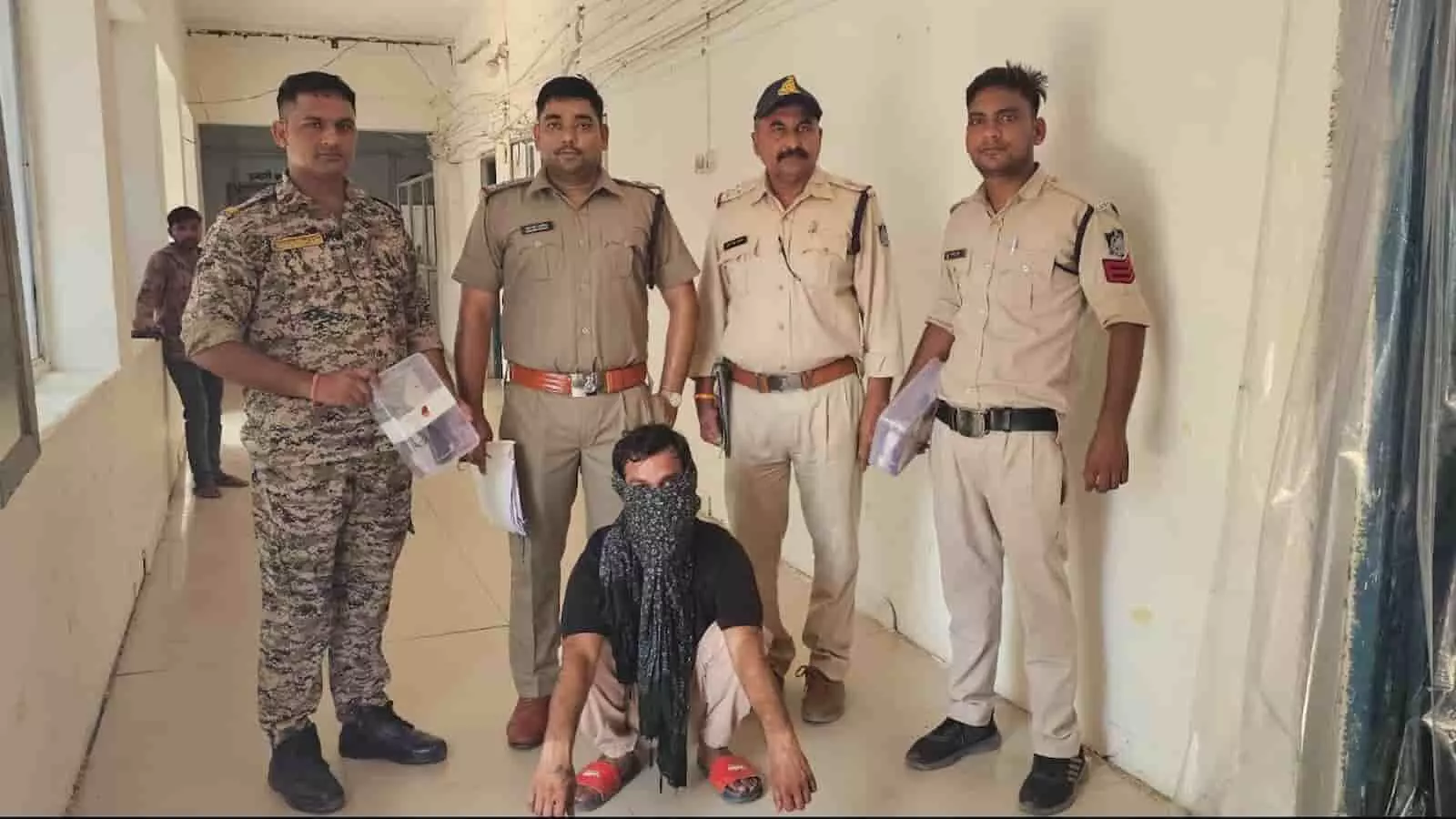 तस्वीर में पुलिसकर्मियों की निगरानी में बैठा एक आरोपी पुलिस थाने के गलियारे में दिख रहा है। तस्वीर में पुलिसकर्मियों की निगरानी में बैठा एक आरोपी पुलिस थाने के गलियारे में दिख रहा है।