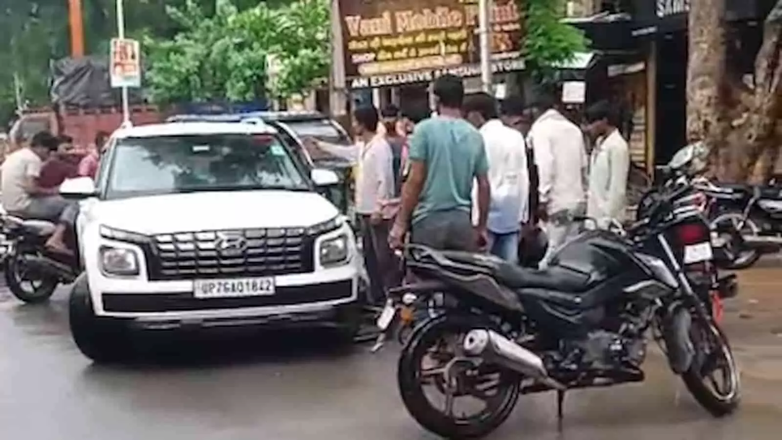 तस्वीर में सड़क पर खड़ी एक कार के पास एकत्रित भीड़ का दृश्य दिख रहा है। तस्वीर में सड़क पर खड़ी एक कार के पास एकत्रित भीड़ का दृश्य दिख रहा है।