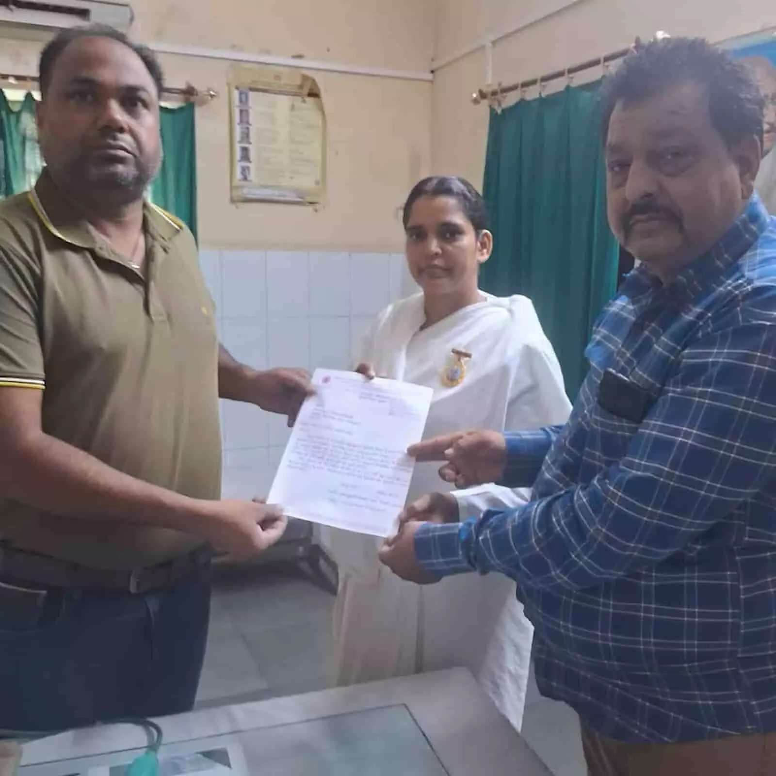 तस्वीर में कमरे के भीतर तीन लोग हाथ में दस्तावेज थामे हुए खड़े दिखाई दे रहे हैं।