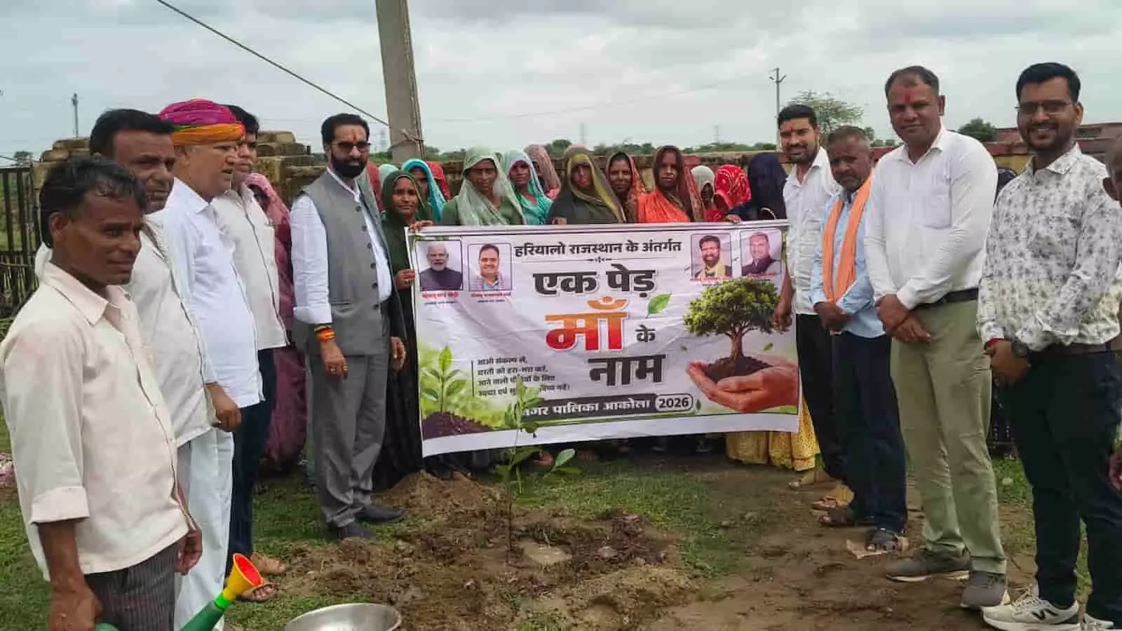 आकोला में एक पेड़ माँ के नाम अभियान बैनर के साथ पौधरोपण करते जनप्रतिनिधि और स्थानीय लोग।