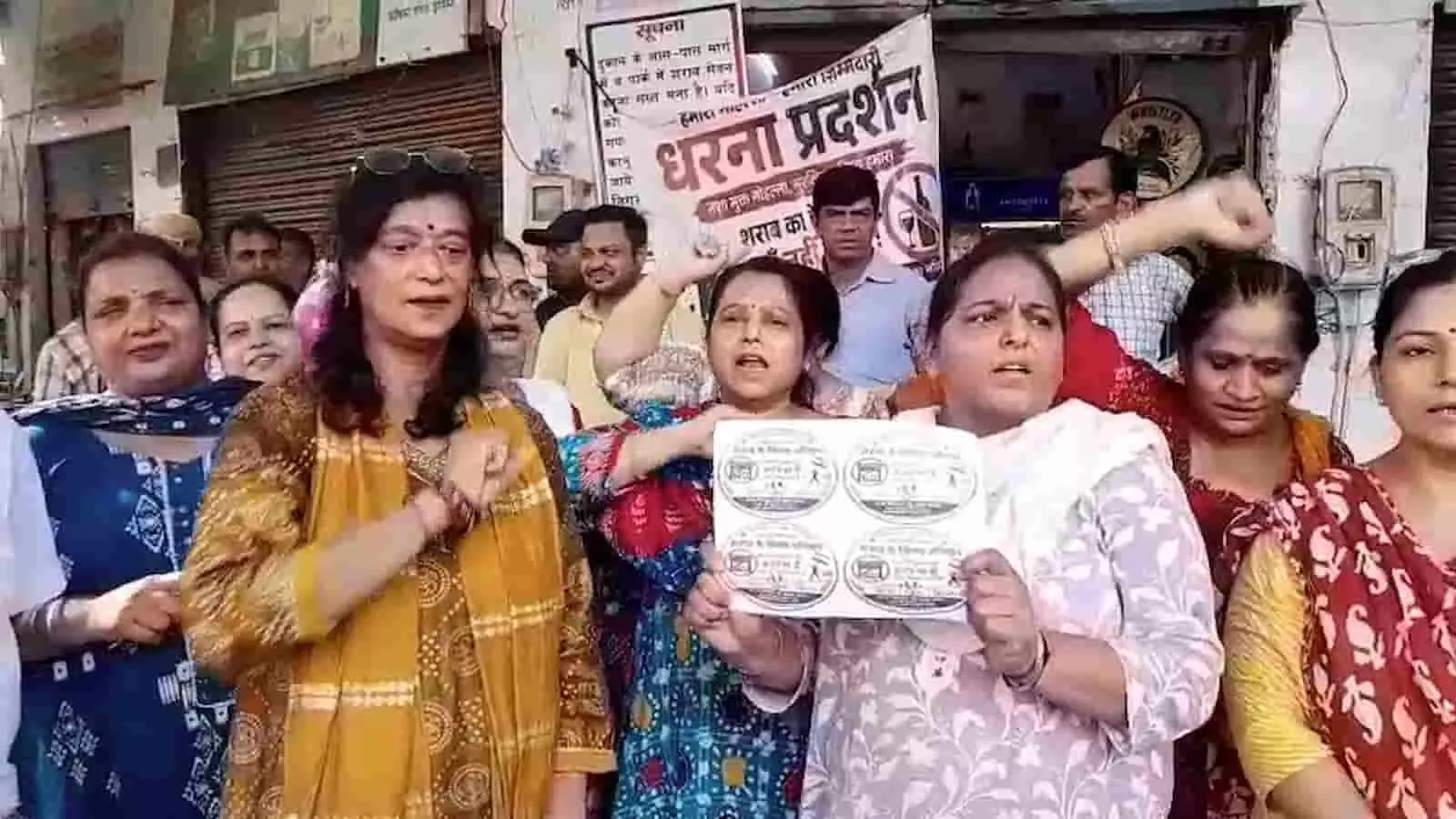 पोस्टर हाथ में लेकर शराब की दुकान के बाहर विरोध प्रदर्शन करतीं स्थानीय महिलाएं। पोस्टर हाथ में लेकर शराब की दुकान के बाहर विरोध प्रदर्शन करतीं स्थानीय महिलाएं।