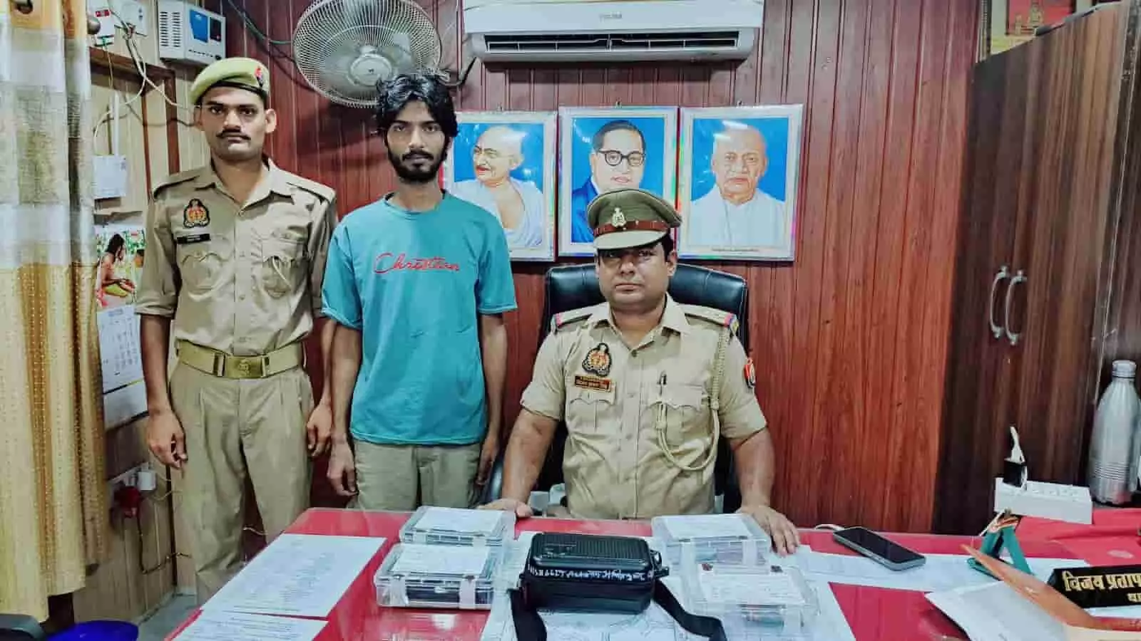 तस्वीर में पुलिस अधिकारी और जवान के साथ खड़ा गिरफ्तार आरोपी मेज पर रखे सामान के पास दिख रहा है। तस्वीर में पुलिस अधिकारी और जवान के साथ खड़ा गिरफ्तार आरोपी मेज पर रखे सामान के पास दिख रहा है।