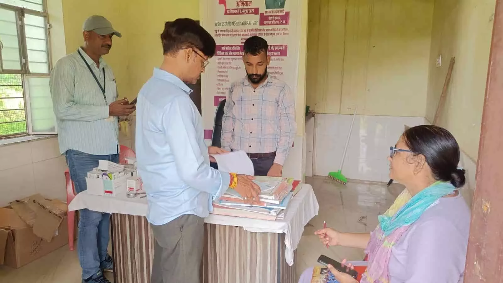 तस्वीर में स्वास्थ्य केंद्र के कमरे में स्वास्थ्य अधिकारी मेज पर रखे रजिस्टरों की जांच करते दिख रहे हैं। तस्वीर में स्वास्थ्य केंद्र के कमरे में स्वास्थ्य अधिकारी मेज पर रखे रजिस्टरों की जांच करते दिख रहे हैं।