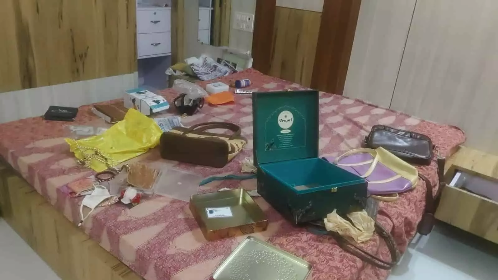 तस्वीर में एक कमरे के बिस्तर पर खुले हुए डिब्बे और बिखरा सामान दिखाई दे रहा है। तस्वीर में एक कमरे के बिस्तर पर खुले हुए डिब्बे और बिखरा सामान दिखाई दे रहा है।