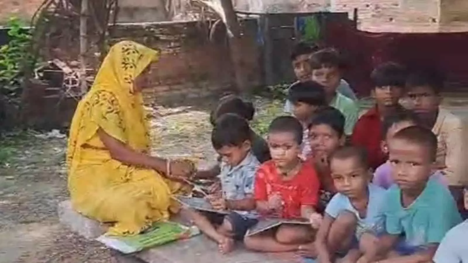 खुले स्थान में नीचे बैठकर पढ़ते बच्चे और उनके सामने बैठी आंगनबाड़ी कार्यकर्ता की तस्वीर। खुले स्थान में नीचे बैठकर पढ़ते बच्चे और उनके सामने बैठी आंगनबाड़ी कार्यकर्ता की तस्वीर।