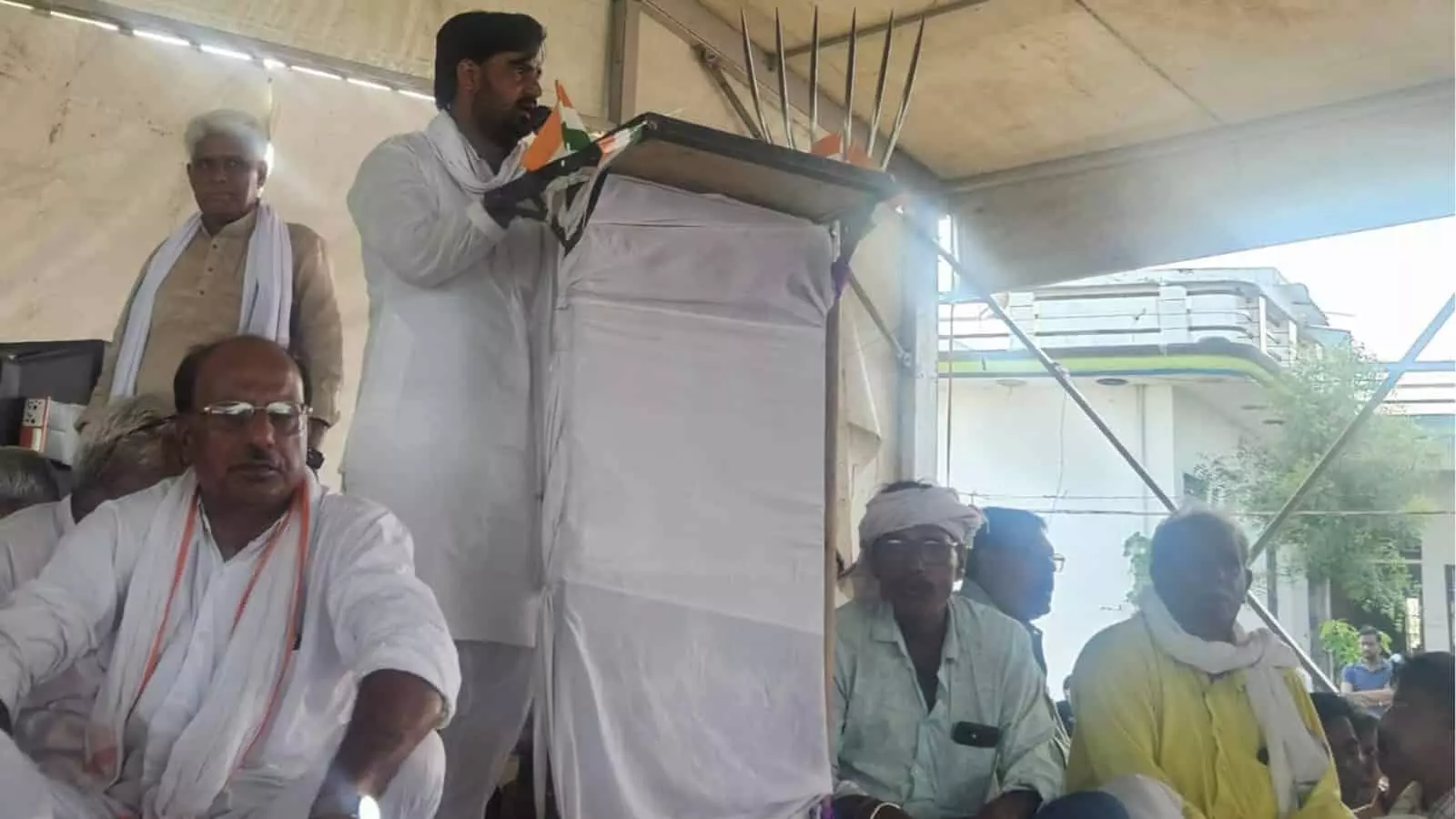 तस्वीर में किसान महापंचायत के दौरान पोडियम से भाषण देते वक्ता और मंच पर बैठे लोग। तस्वीर में किसान महापंचायत के दौरान पोडियम से भाषण देते वक्ता और मंच पर बैठे लोग।