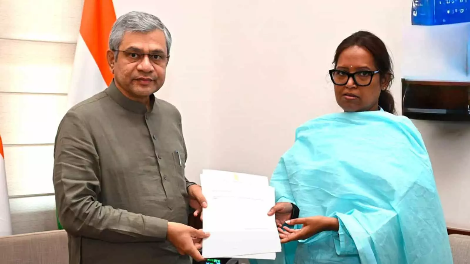 तस्वीर में एक कमरे के भीतर दो लोग मिलकर एक आधिकारिक दस्तावेज पकड़े हुए दिख रहे हैं। तस्वीर में एक कमरे के भीतर दो लोग मिलकर एक आधिकारिक दस्तावेज पकड़े हुए दिख रहे हैं।