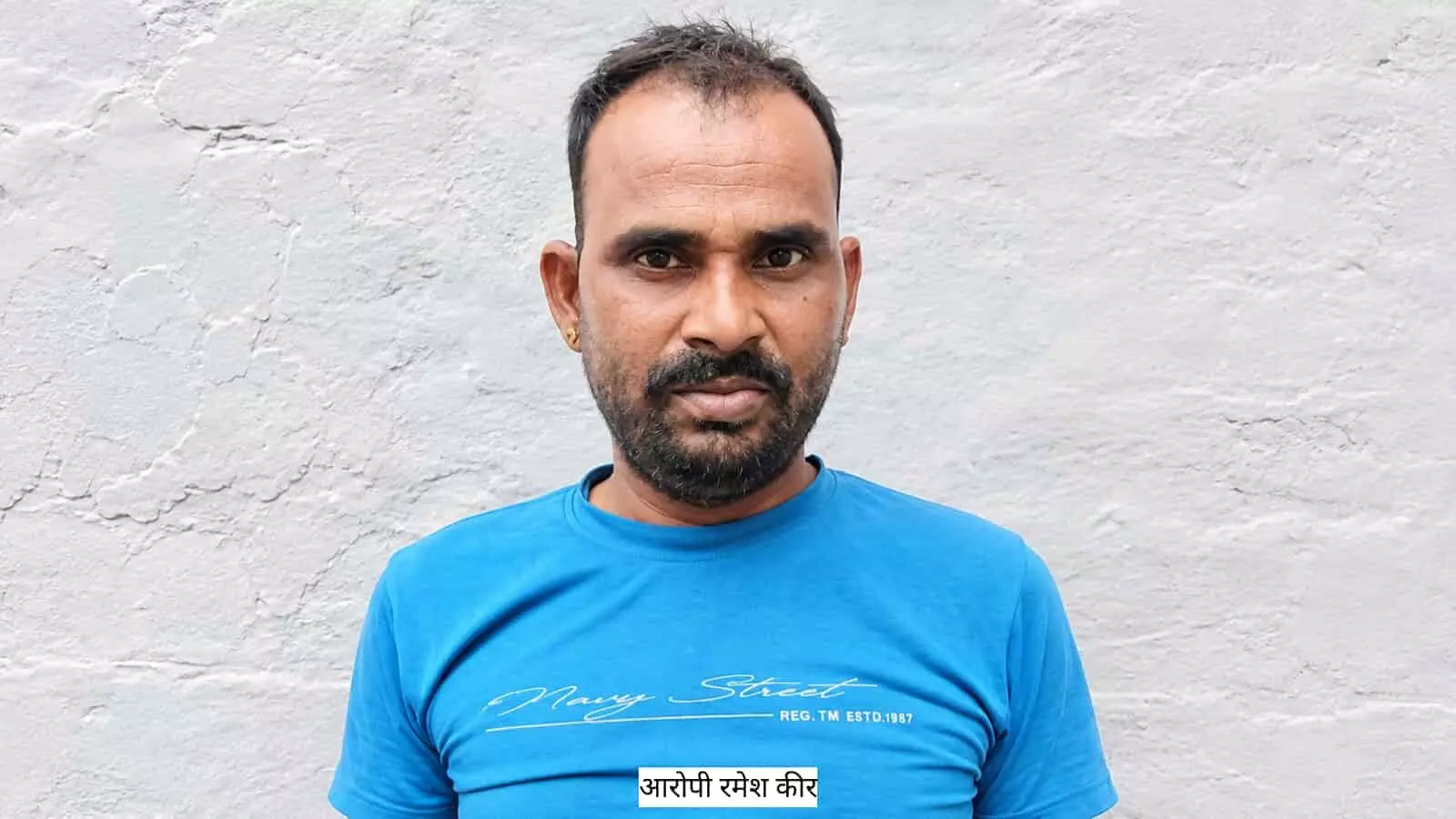 तस्वीर में दिख रहा व्यक्ति सफेद रंग की दीवार के सामने नीली टी-शर्ट पहने खड़ा है। तस्वीर में दिख रहा व्यक्ति सफेद रंग की दीवार के सामने नीली टी-शर्ट पहने खड़ा है।