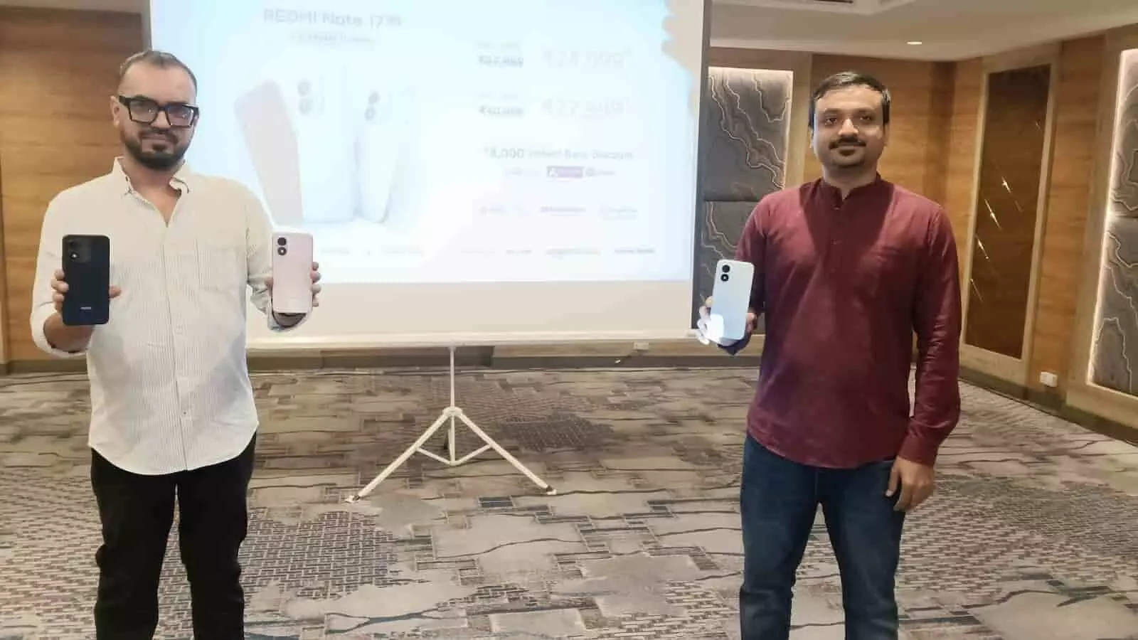 तस्वीर में दो व्यक्ति स्टेज पर प्रोजेक्टर स्क्रीन के आगे खड़े होकर नए स्मार्टफोन प्रदर्शित कर रहे हैं। तस्वीर में दो व्यक्ति स्टेज पर प्रोजेक्टर स्क्रीन के आगे खड़े होकर नए स्मार्टफोन प्रदर्शित कर रहे हैं।