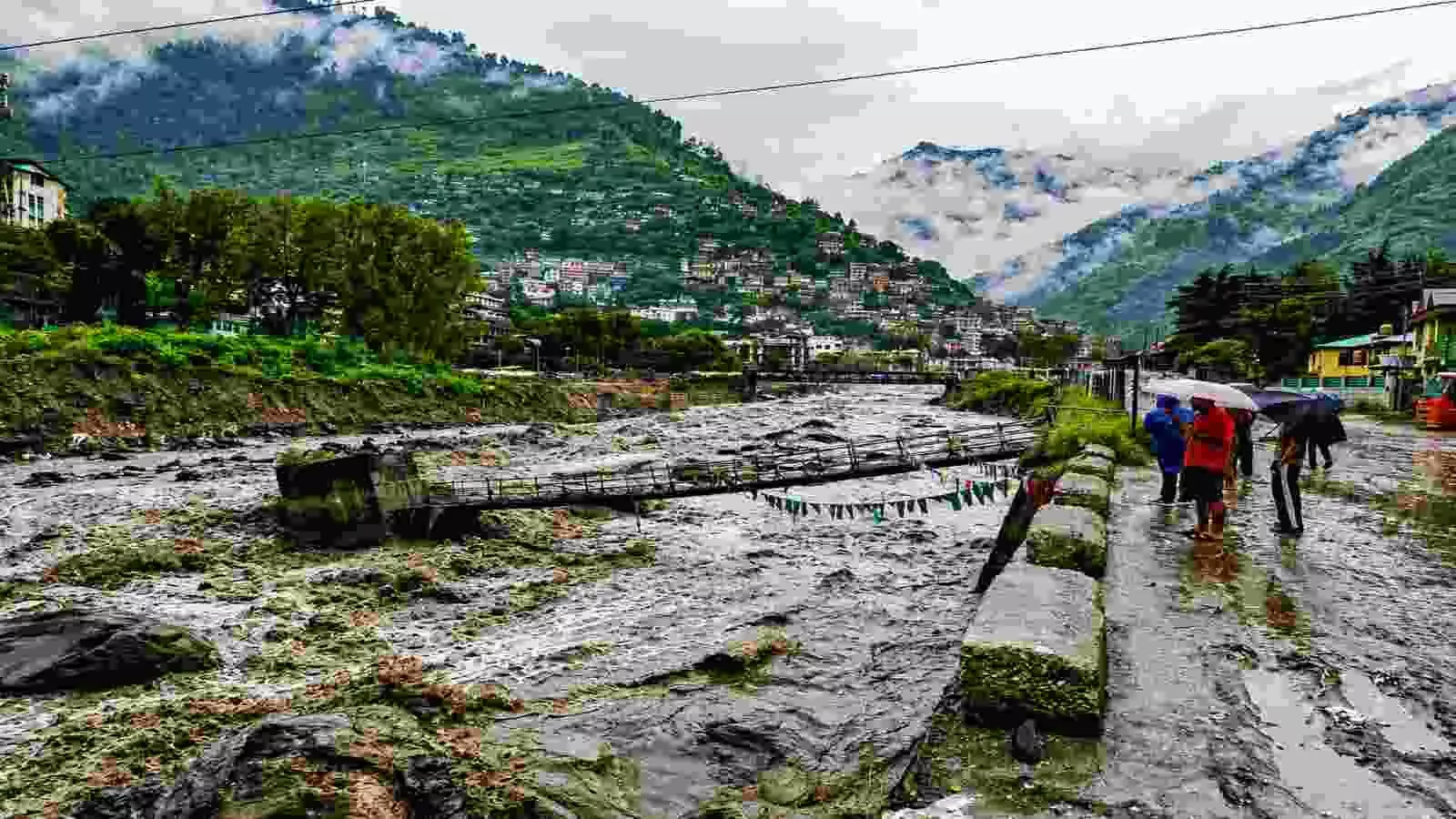 बादलों से घिरे पहाड़ों के बीच उफनती नदी और सड़क पर खड़े लोग उत्तर भारत में भारी बारिश की चेतावनी को दर्शा रहे हैं। बादलों से घिरे पहाड़ों के बीच उफनती नदी और सड़क पर खड़े लोग उत्तर भारत में भारी बारिश की चेतावनी को दर्शा रहे हैं।